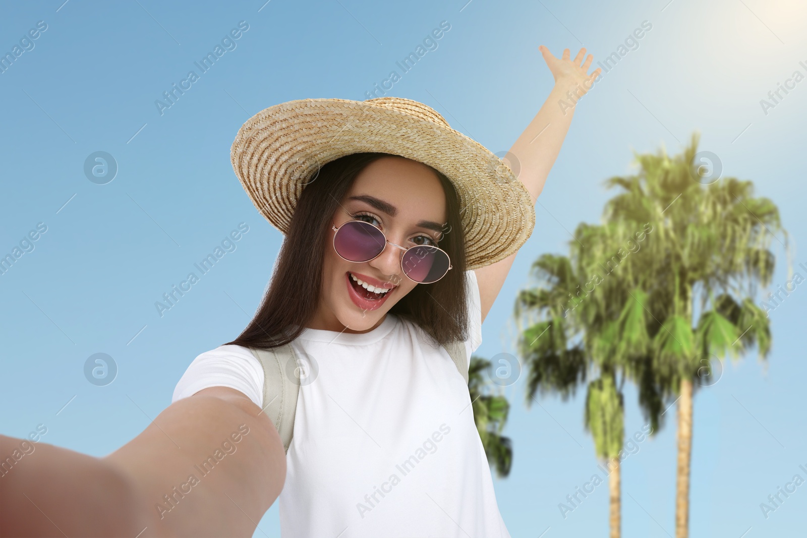 Image of Happy woman in straw hat taking selfie near palms