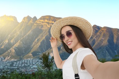 Happy woman in straw hat taking selfie in mountains