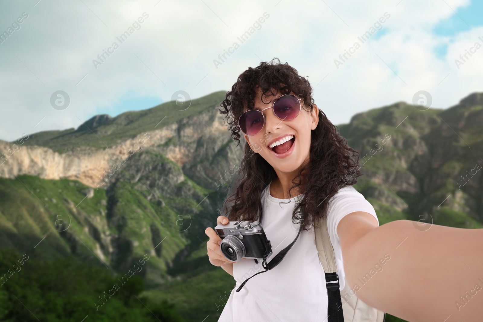 Image of Beautiful woman with sunglasses and camera taking selfie in mountains