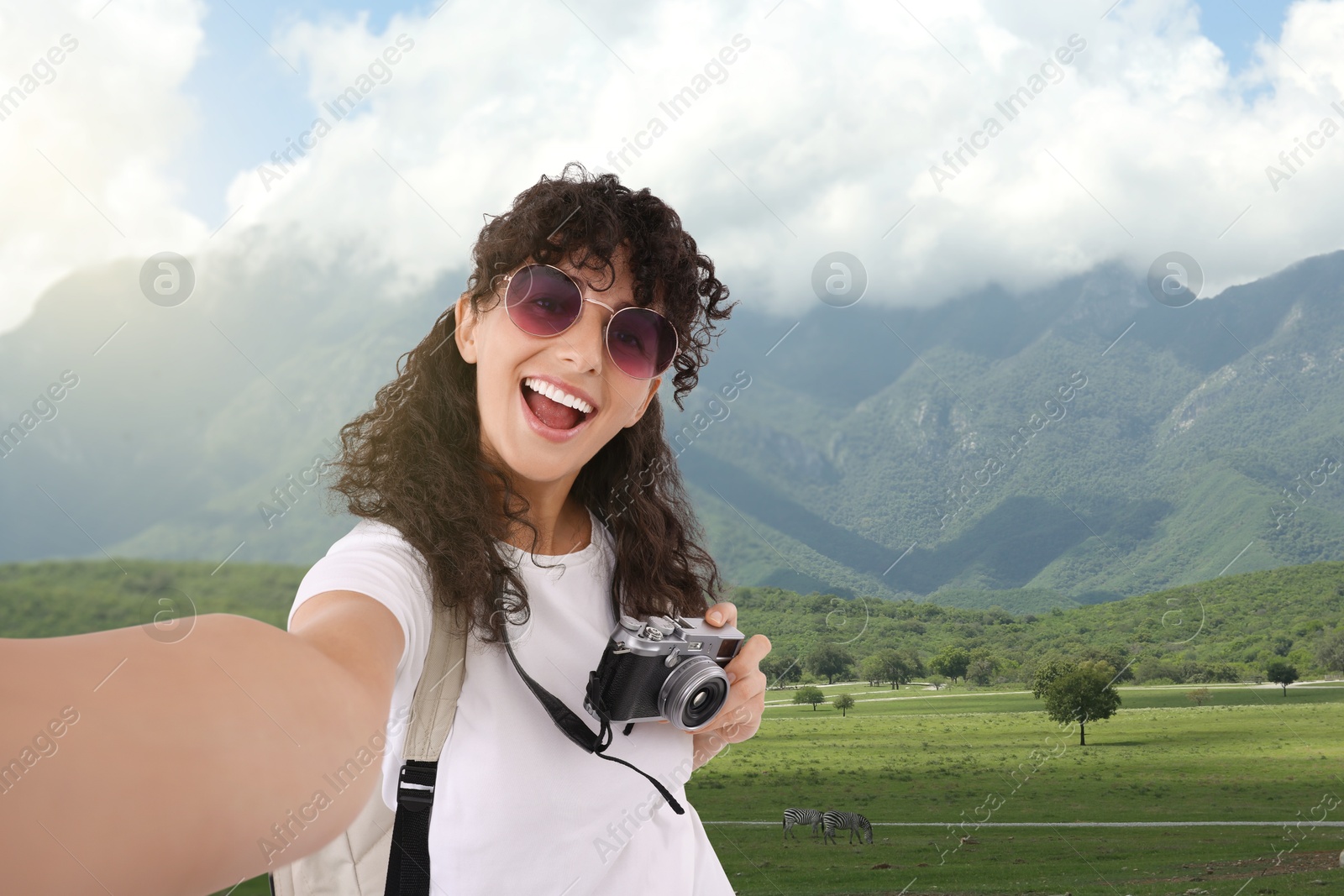 Image of Beautiful woman with sunglasses and camera taking selfie in mountains