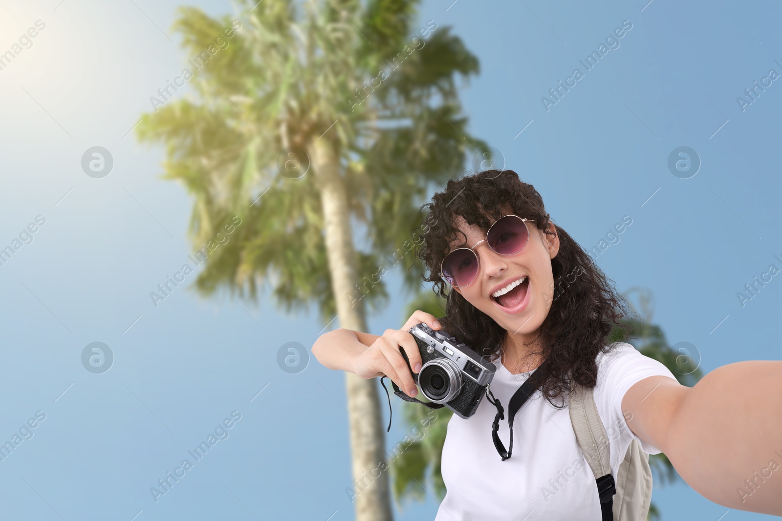 Image of Beautiful woman with sunglasses and camera taking selfie against palm