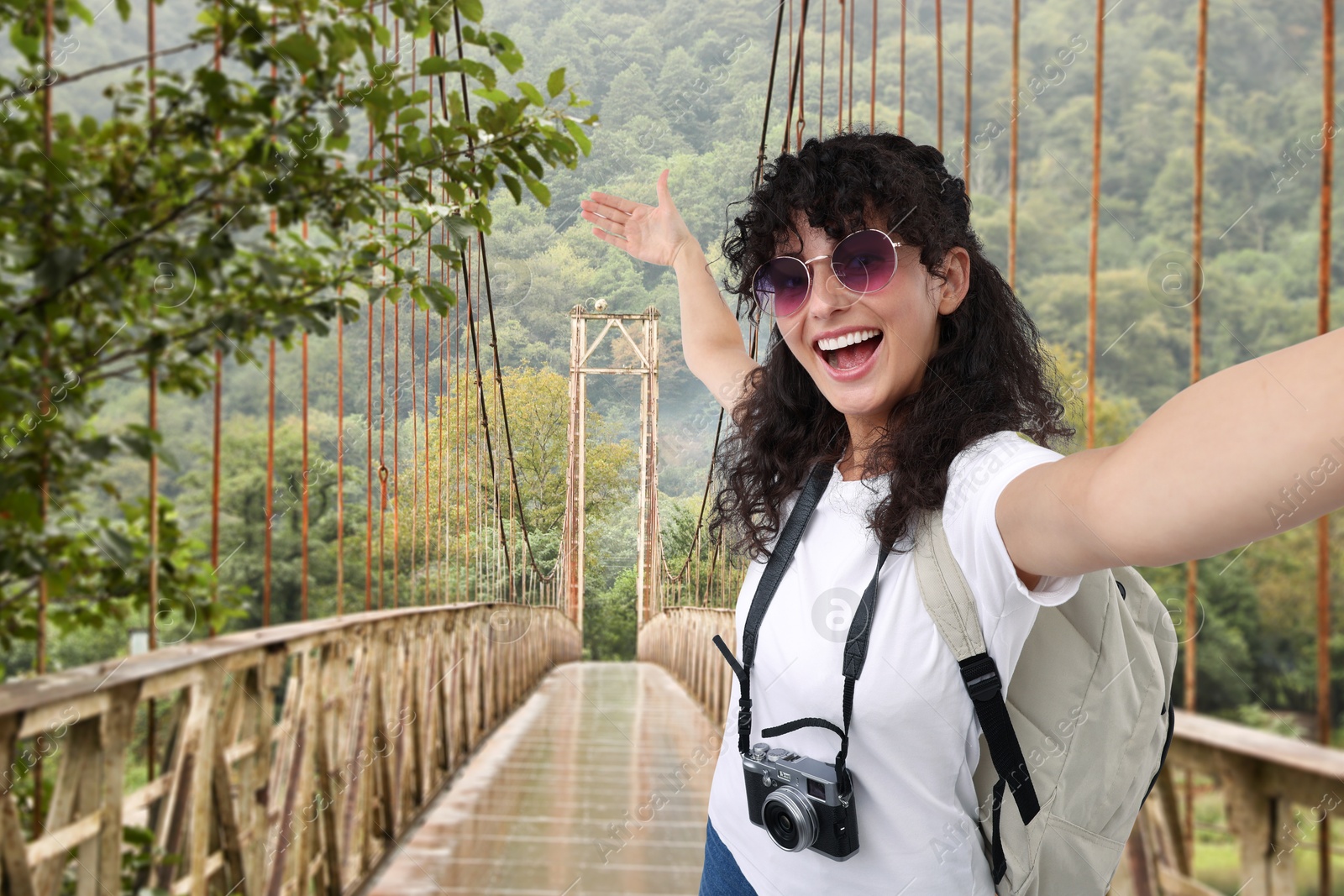 Image of Beautiful woman with sunglasses and camera taking selfie on suspended bridge