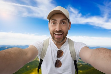 Image of Happy man with cap and sunglasses taking selfie in mountains