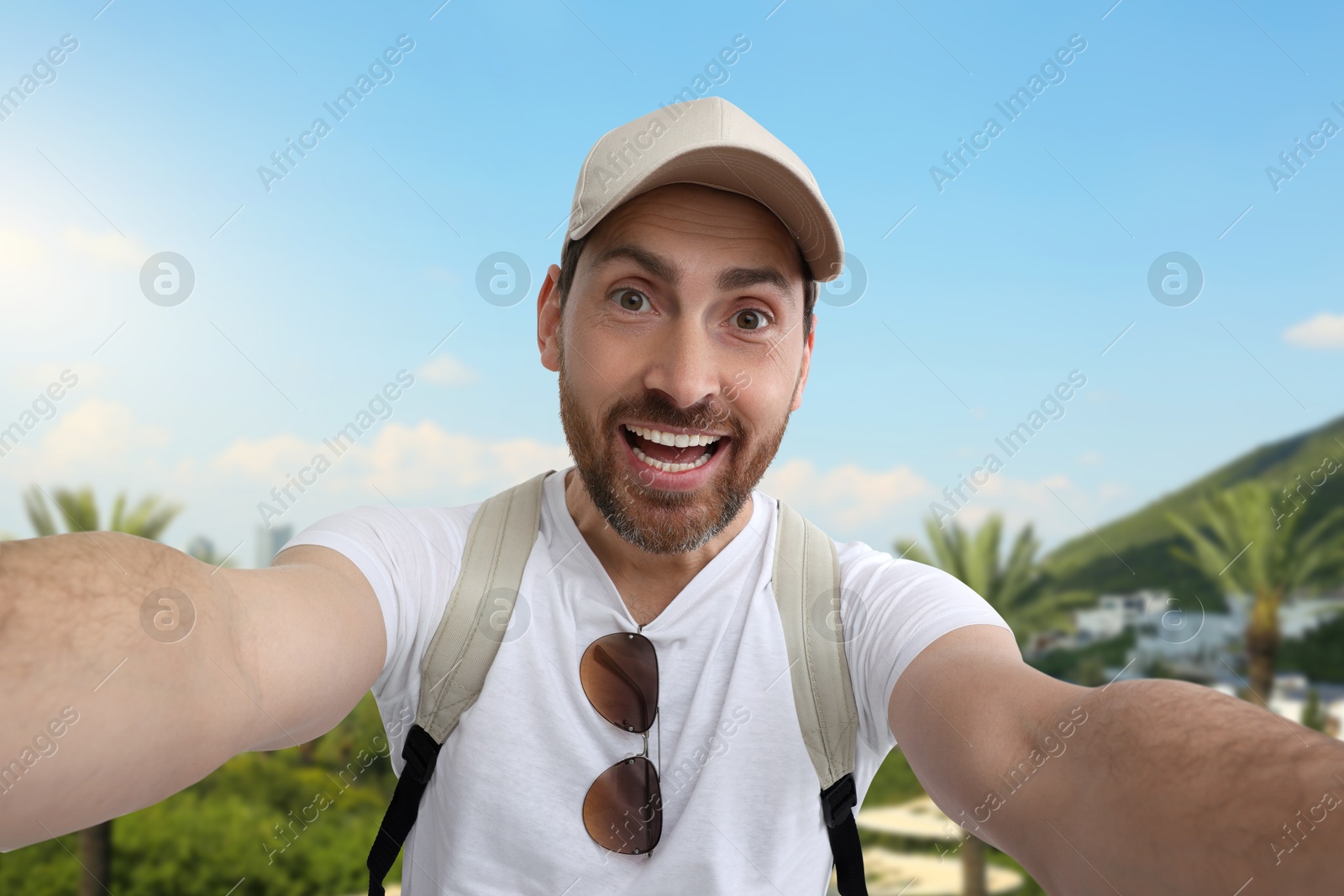 Image of Happy man with cap and sunglasses taking selfie in nature