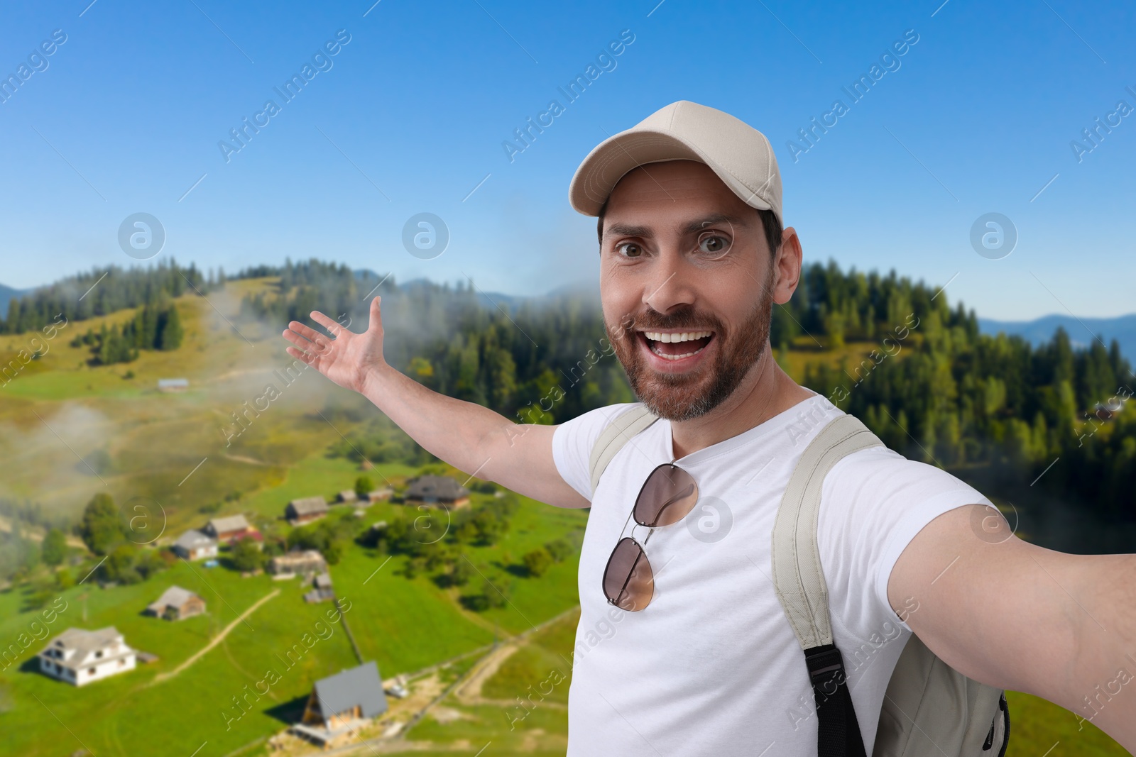 Image of Happy man with cap and sunglasses taking selfie in mountains