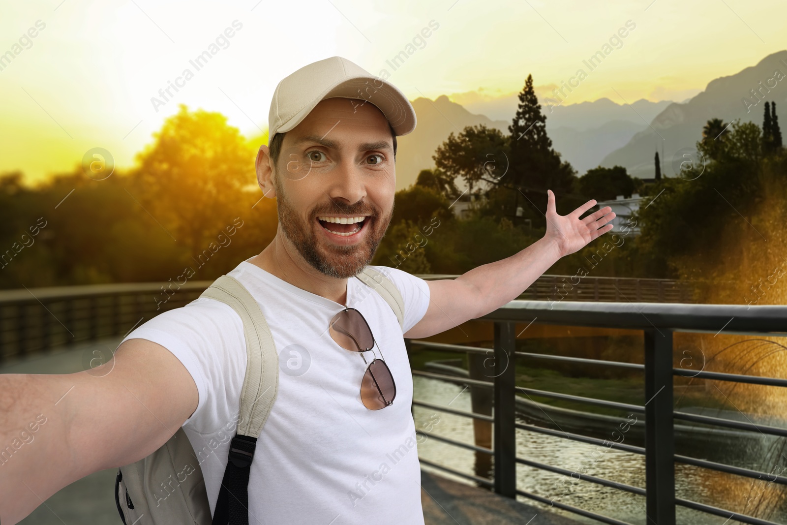 Image of Happy man with cap and sunglasses taking selfie in park