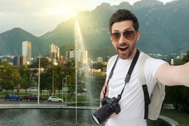 Image of Happy man with sunglasses and camera taking selfie in city