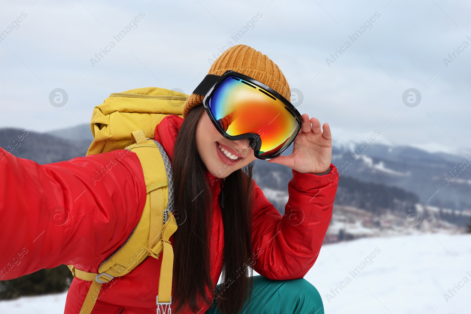 Image of Happy young woman with ski goggles taking selfie in mountains