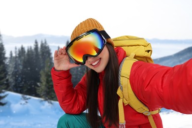 Happy young woman with ski goggles taking selfie in mountains