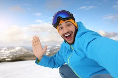 Happy young man with ski goggles taking selfie in mountains