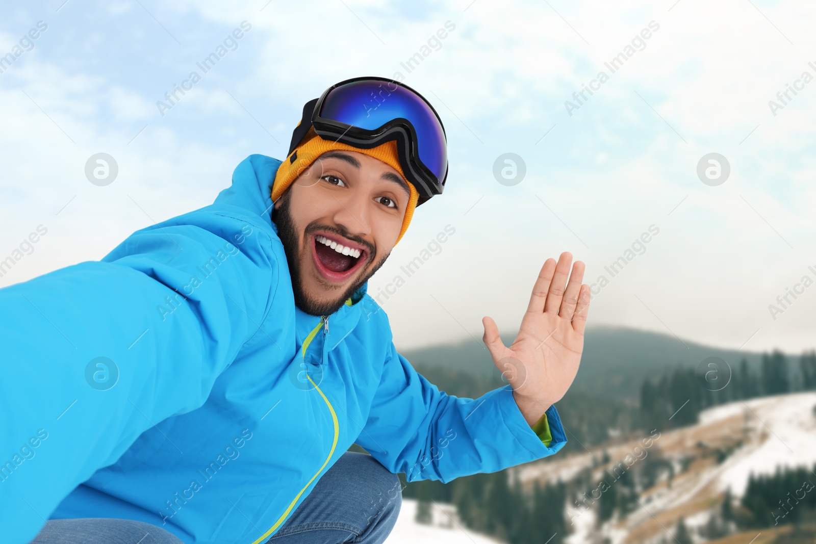 Image of Happy young man with ski goggles taking selfie in mountains