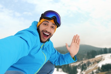 Happy young man with ski goggles taking selfie in mountains