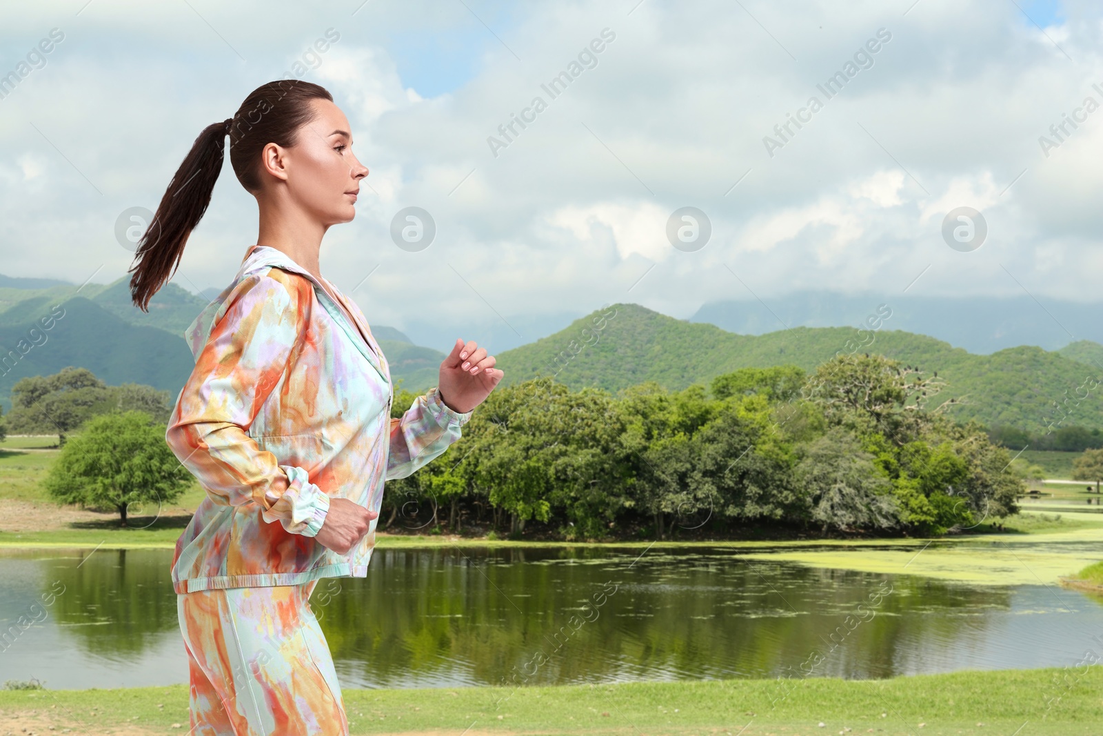 Image of Sporty woman running on meadow near lake. Space for text