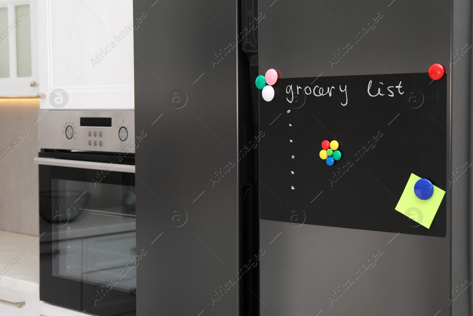 Photo of Magnetic board with grocery list and note on refrigerator in kitchen