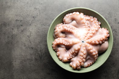 Photo of Raw octopus in bowl on grey textured table, top view. Space for text