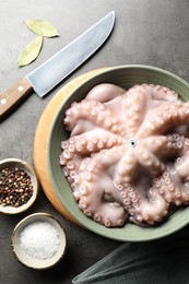 Photo of Raw octopus in bowl, peppercorns and salt on grey textured table, flat lay