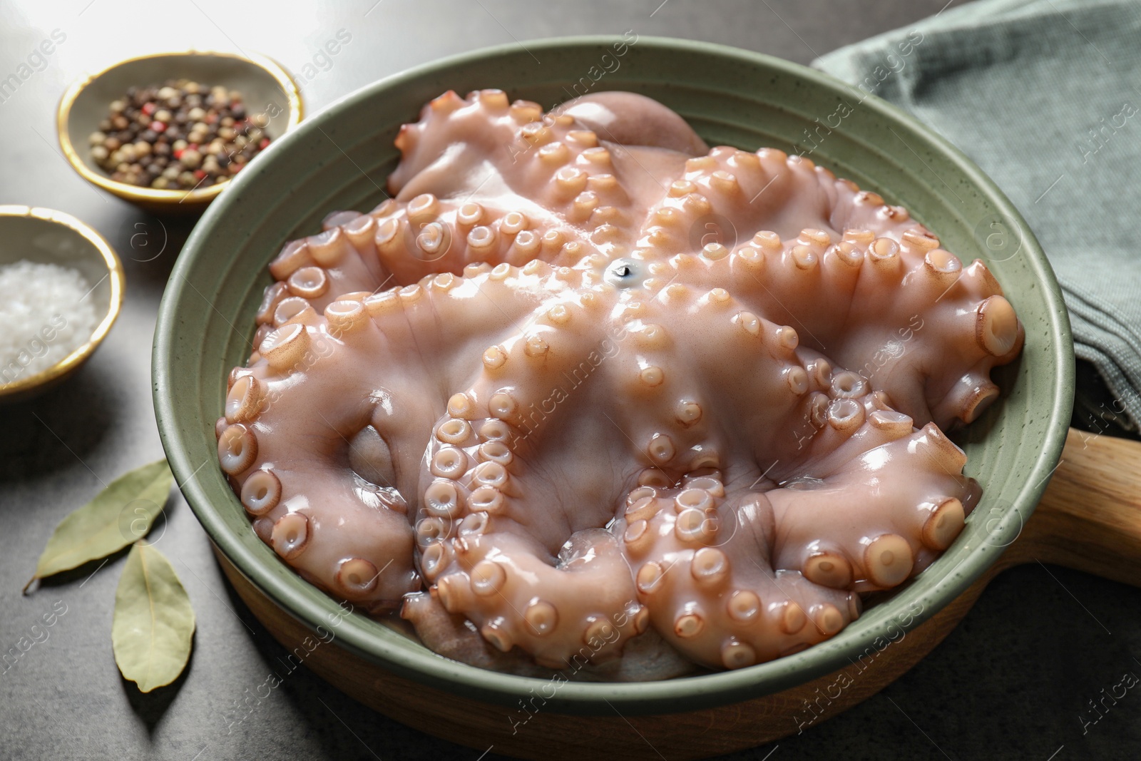 Photo of Raw octopus in bowl and spices on grey textured table, closeup