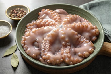 Raw octopus in bowl and spices on grey textured table, closeup