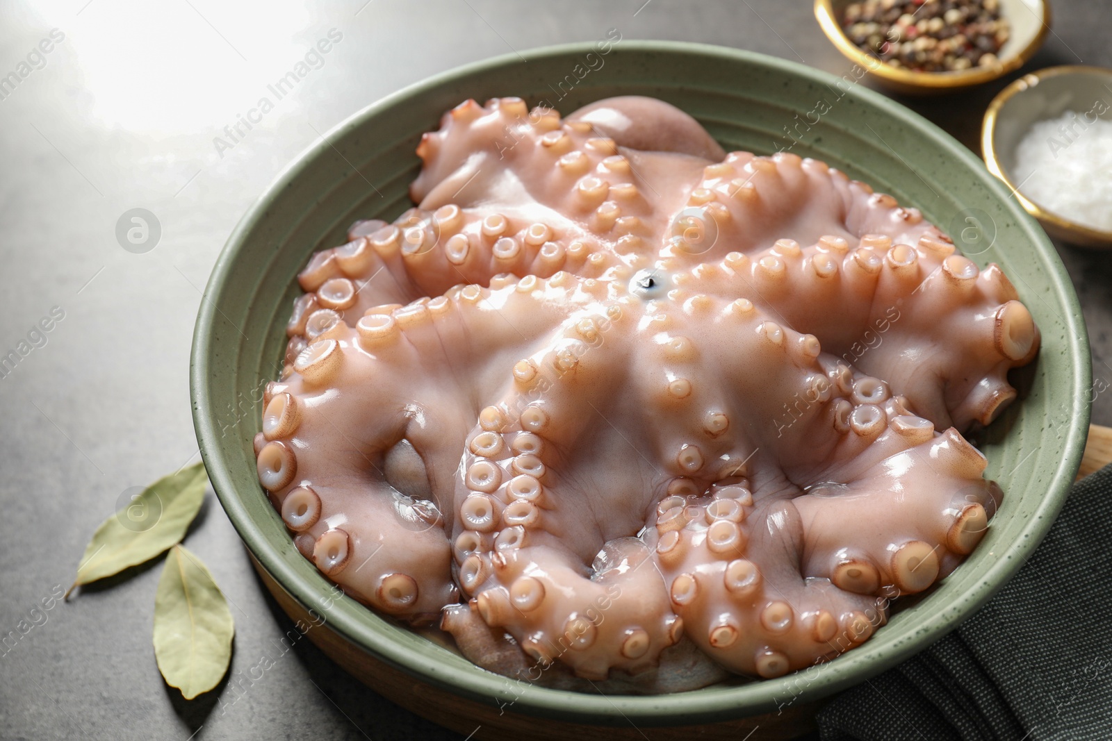 Photo of Raw octopus in bowl and spices on grey textured table, closeup