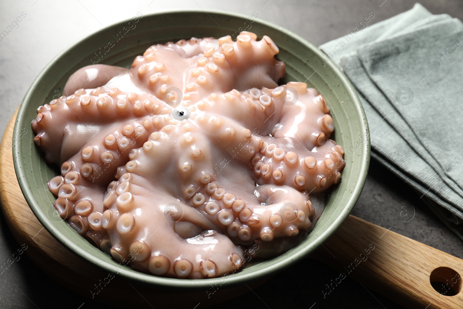 Photo of Raw octopus in bowl and napkin on grey textured table, closeup