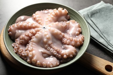 Photo of Raw octopus in bowl and napkin on grey textured table, closeup