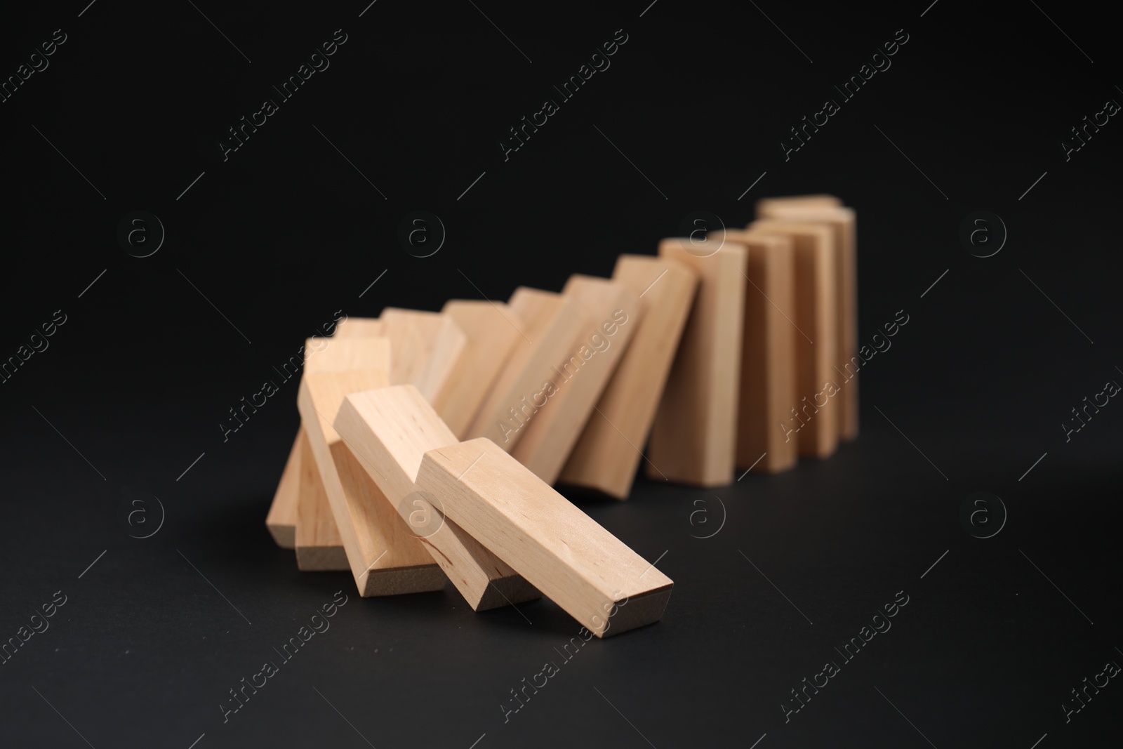 Photo of Domino effect. Wooden blocks falling on black background