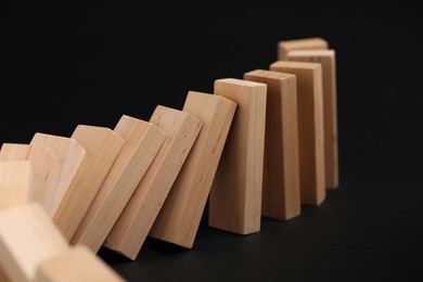 Photo of Domino effect. Wooden blocks falling on black background, closeup