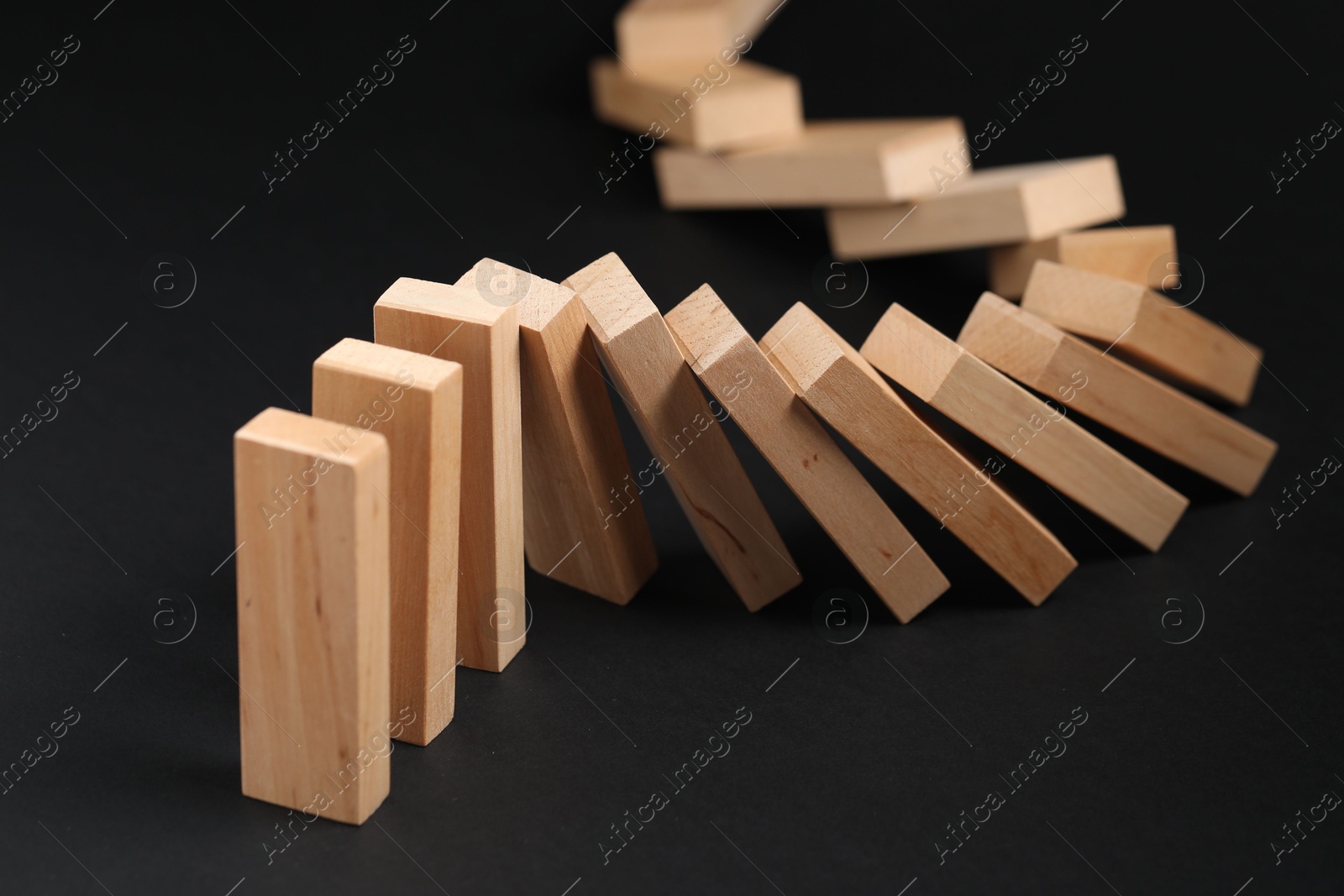 Photo of Domino effect. Wooden blocks falling on black background