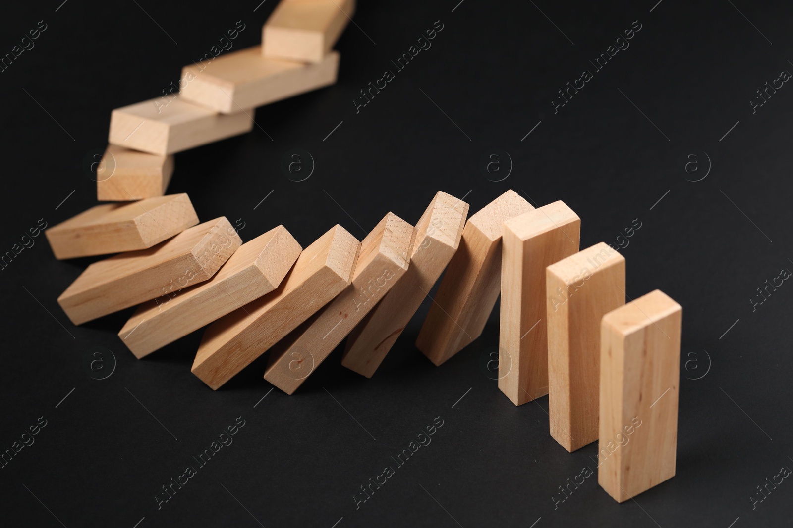 Photo of Domino effect. Wooden blocks falling on black background