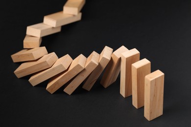 Photo of Domino effect. Wooden blocks falling on black background