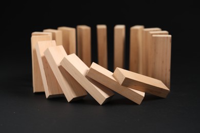 Photo of Domino effect. Wooden blocks falling on black background, closeup