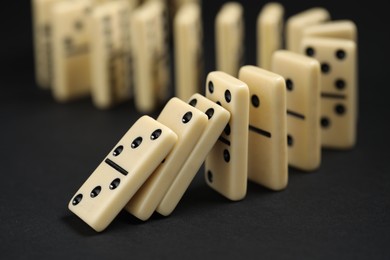 Photo of Domino effect. Tiles falling on black background, closeup