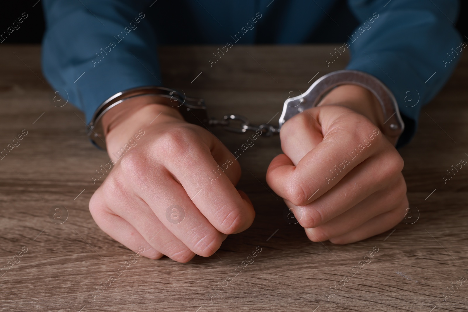 Photo of Woman in metal handcuffs at wooden table, closeup