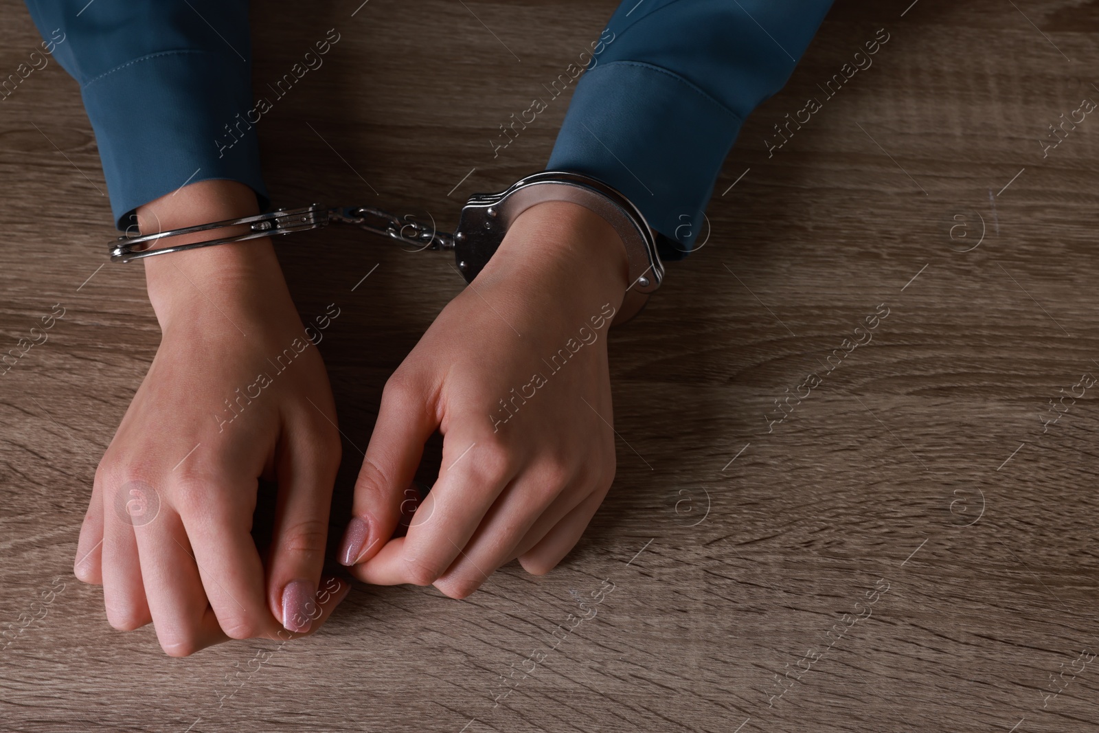 Photo of Woman in metal handcuffs at wooden table, above view