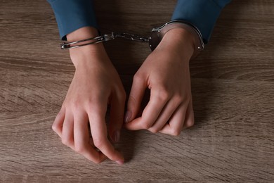 Photo of Woman in metal handcuffs at wooden table, above view