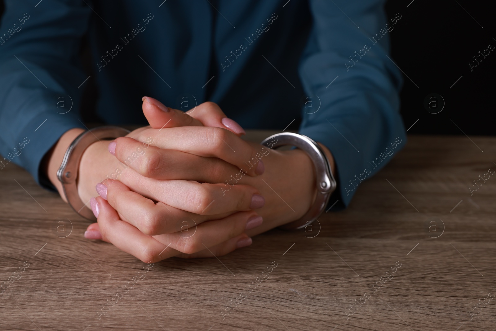 Photo of Woman in metal handcuffs at wooden table, closeup