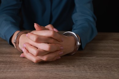 Photo of Woman in metal handcuffs at wooden table, closeup