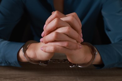 Photo of Woman in metal handcuffs at wooden table, closeup