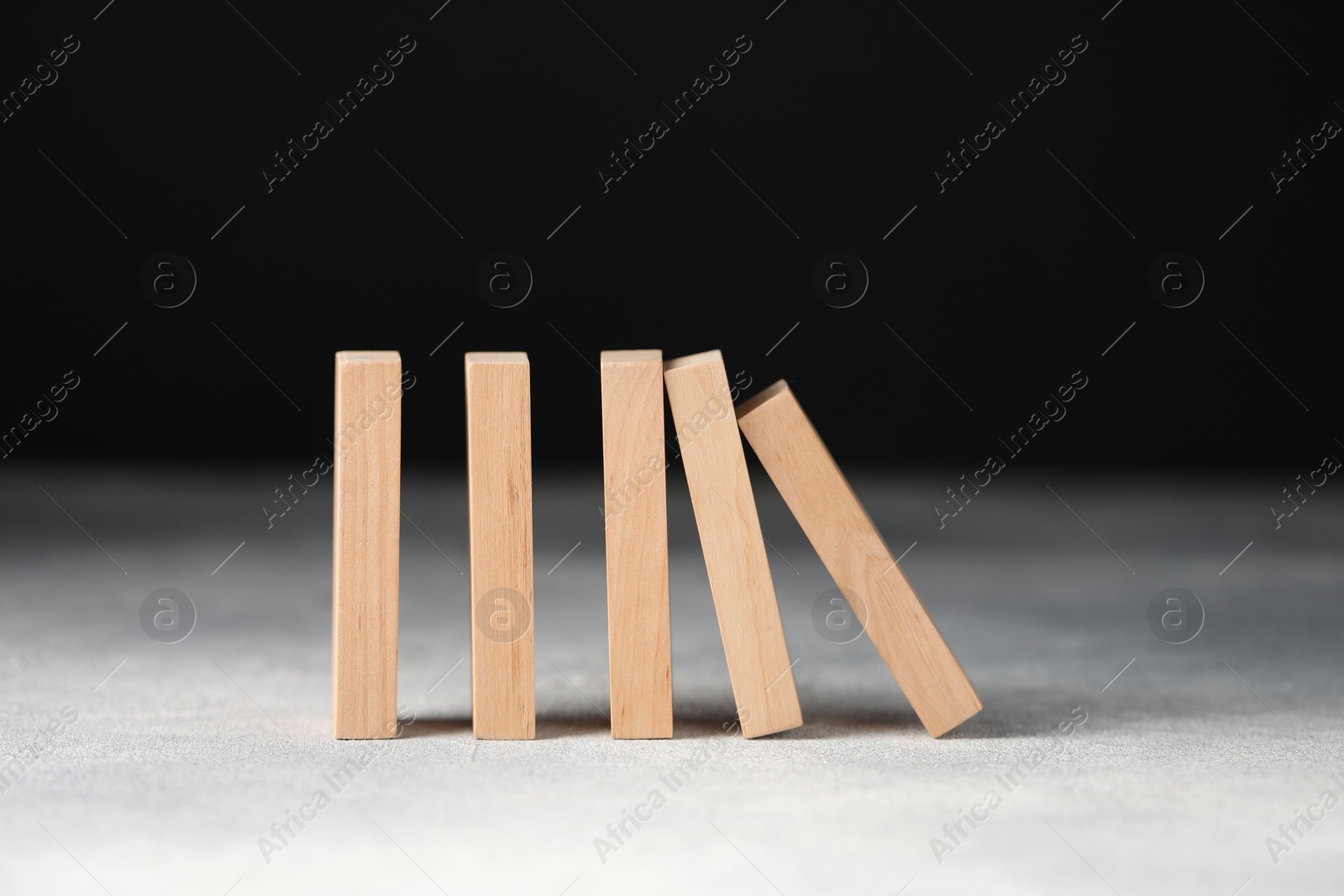 Photo of Domino effect. Wooden blocks falling on light table against black background, closeup