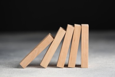 Photo of Domino effect. Wooden blocks falling on light table against black background, closeup