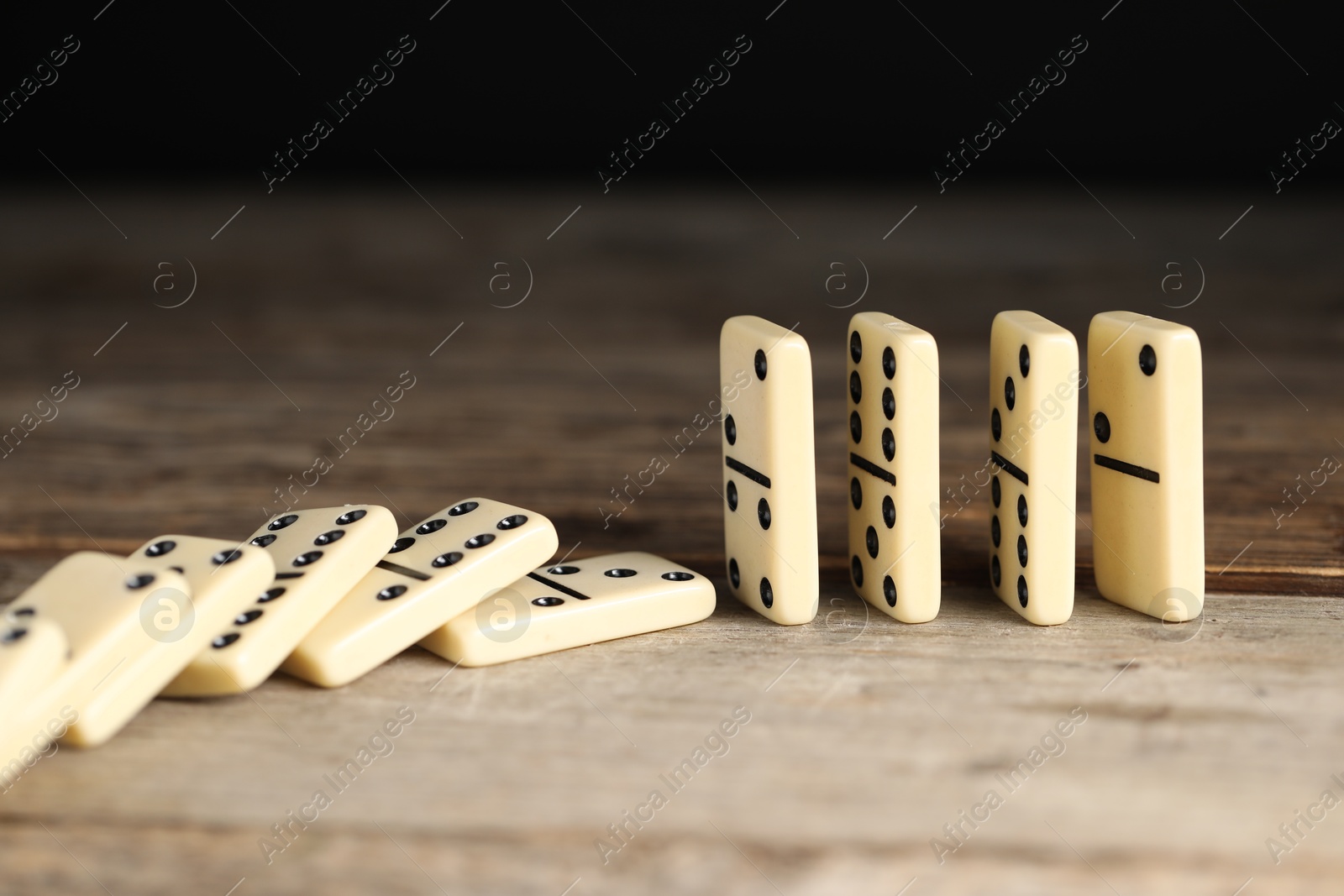 Photo of Domino effect. Tiles falling on wooden table, closeup