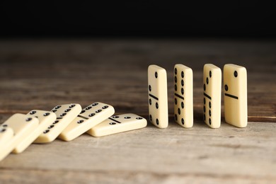 Photo of Domino effect. Tiles falling on wooden table, closeup