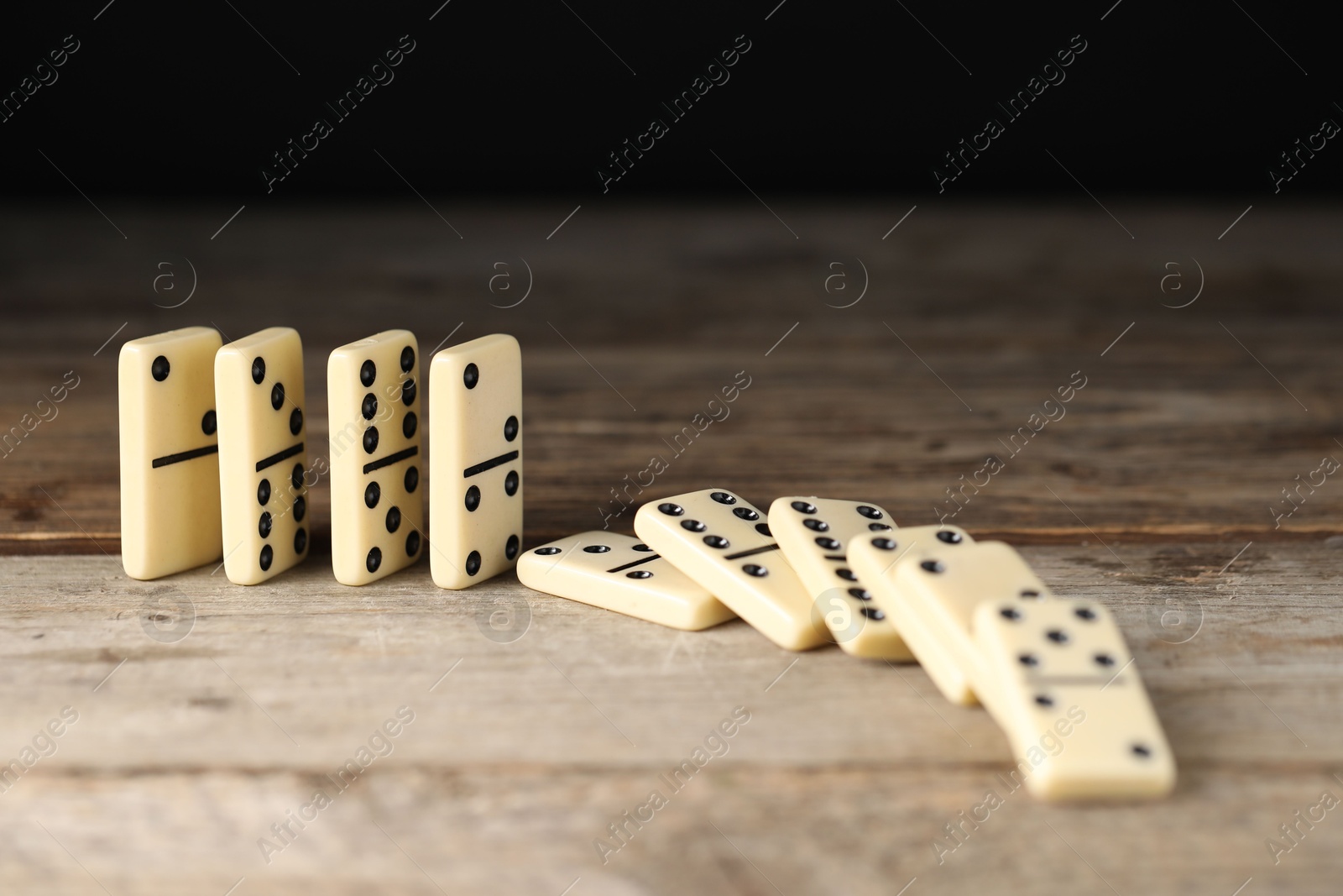 Photo of Domino effect. Tiles falling on wooden table, closeup