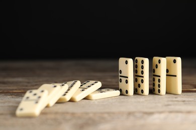 Photo of Domino effect. Tiles falling on wooden table against black background, closeup