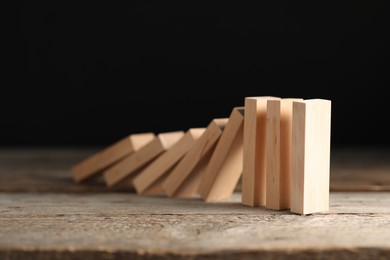 Photo of Domino effect. Wooden blocks falling on table against black background, closeup