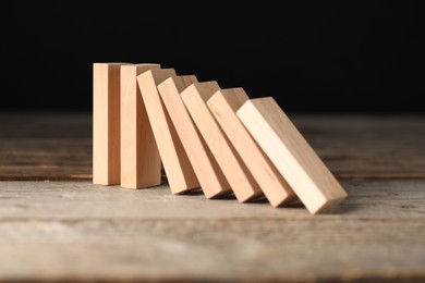 Photo of Domino effect. Wooden blocks falling on table against black background, closeup