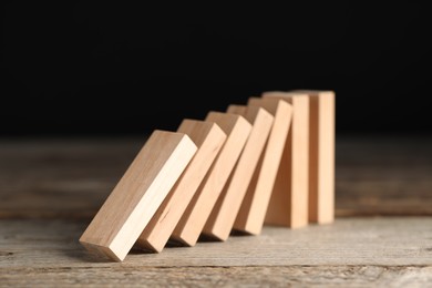 Photo of Domino effect. Wooden blocks falling on table against black background, closeup