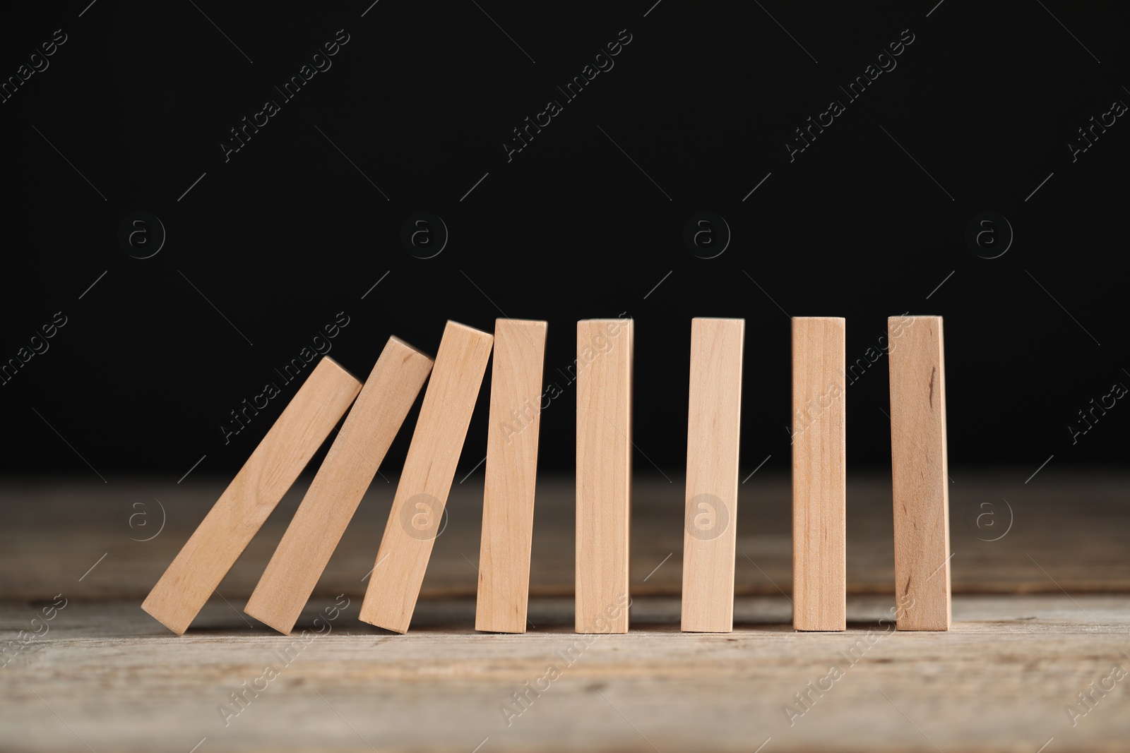 Photo of Domino effect. Wooden blocks falling on table against black background