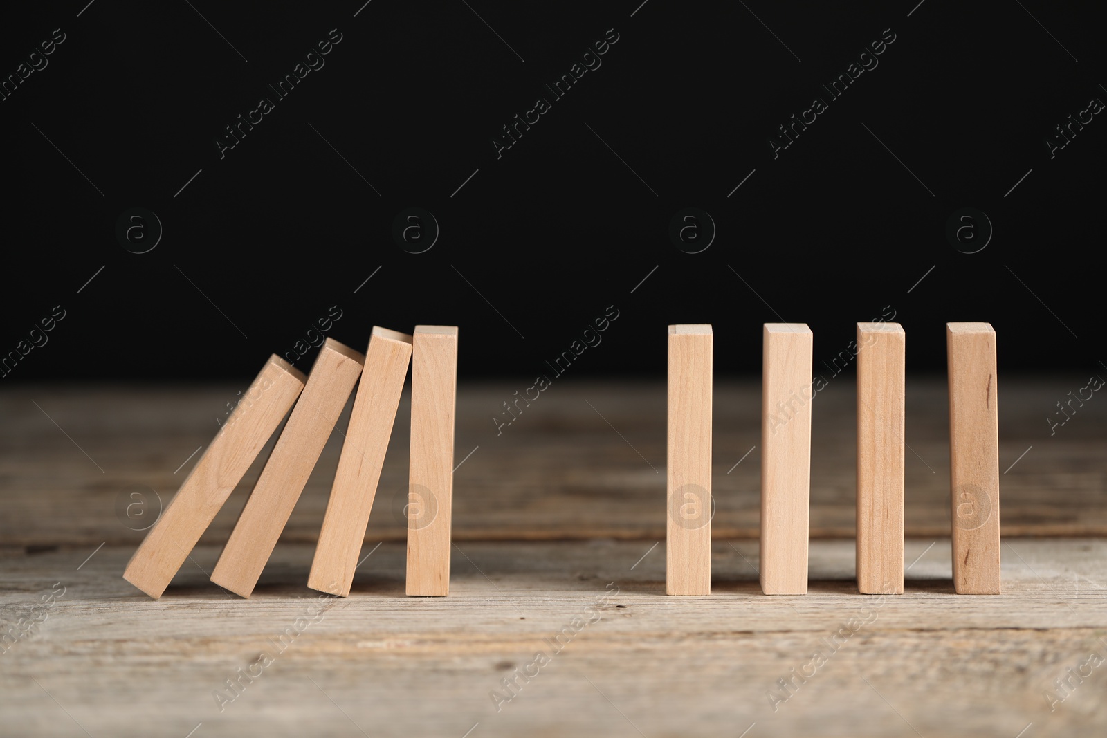 Photo of Domino effect. Wooden blocks falling on table against black background