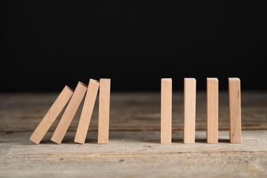 Photo of Domino effect. Wooden blocks falling on table against black background